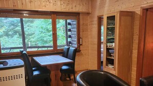A wooden cabin interior with a dining table, chairs, and a kitchen area.