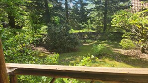 A wooden deck overlooking a forested area with a stone wall and a small stream.