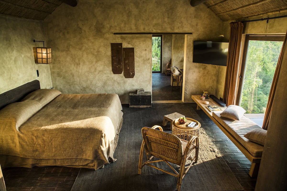 Ein Schlafzimmer mit einem großen Bett, einer hölzernen Bank, einem kleinen Tisch und einem an der Wand befestigten Fernseher.