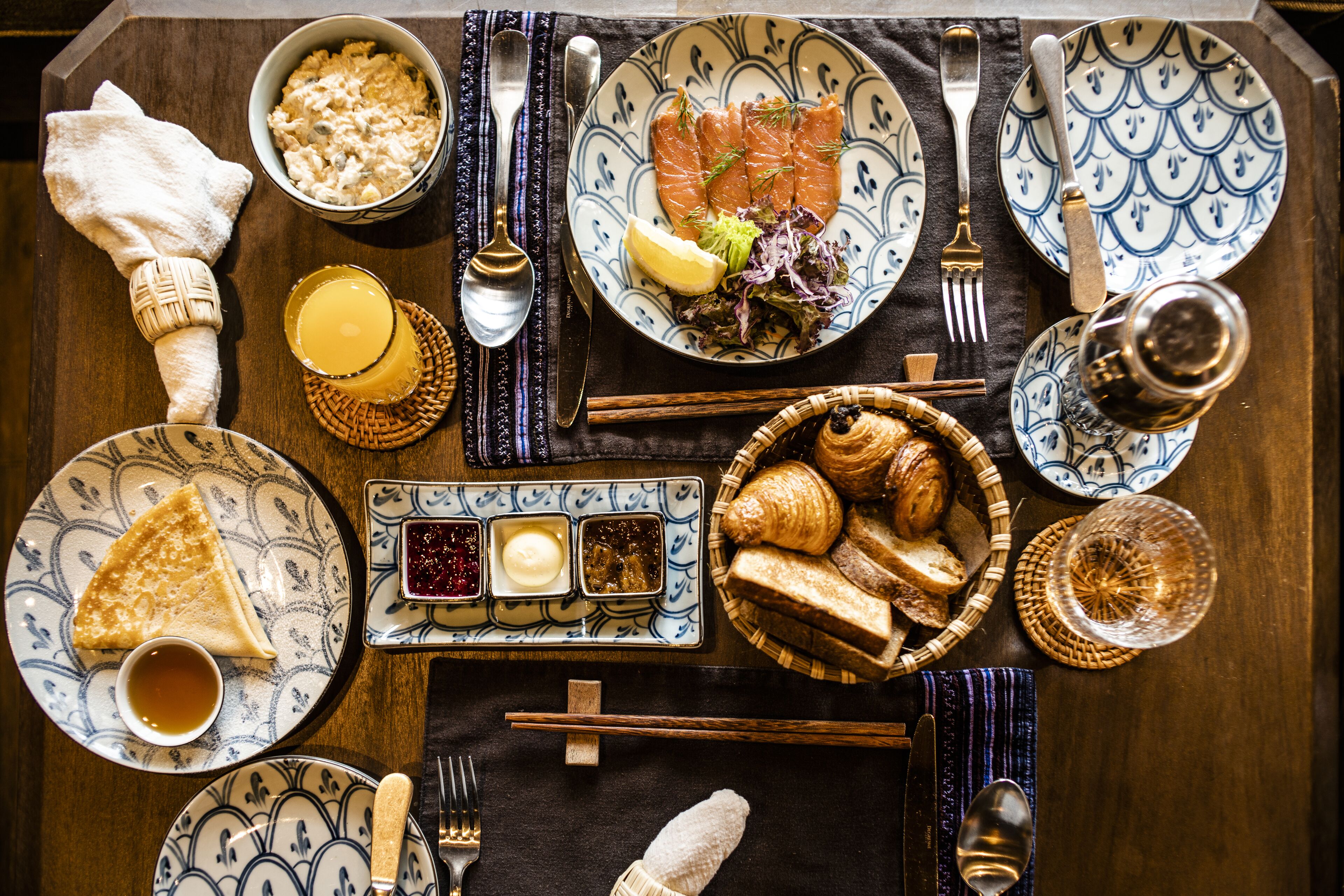 A table set with various dishes including salmon, croissants, and bread, along with condiments and utensils.