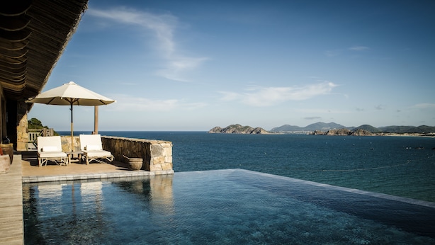 An infinity pool with clear water, a thatched roof structure, and lounge chairs. - Zannier Bãi San Hô (Xuan Canh)