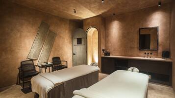 Two single beds with white linens, a desk, and a vanity area with a mirror and sink.