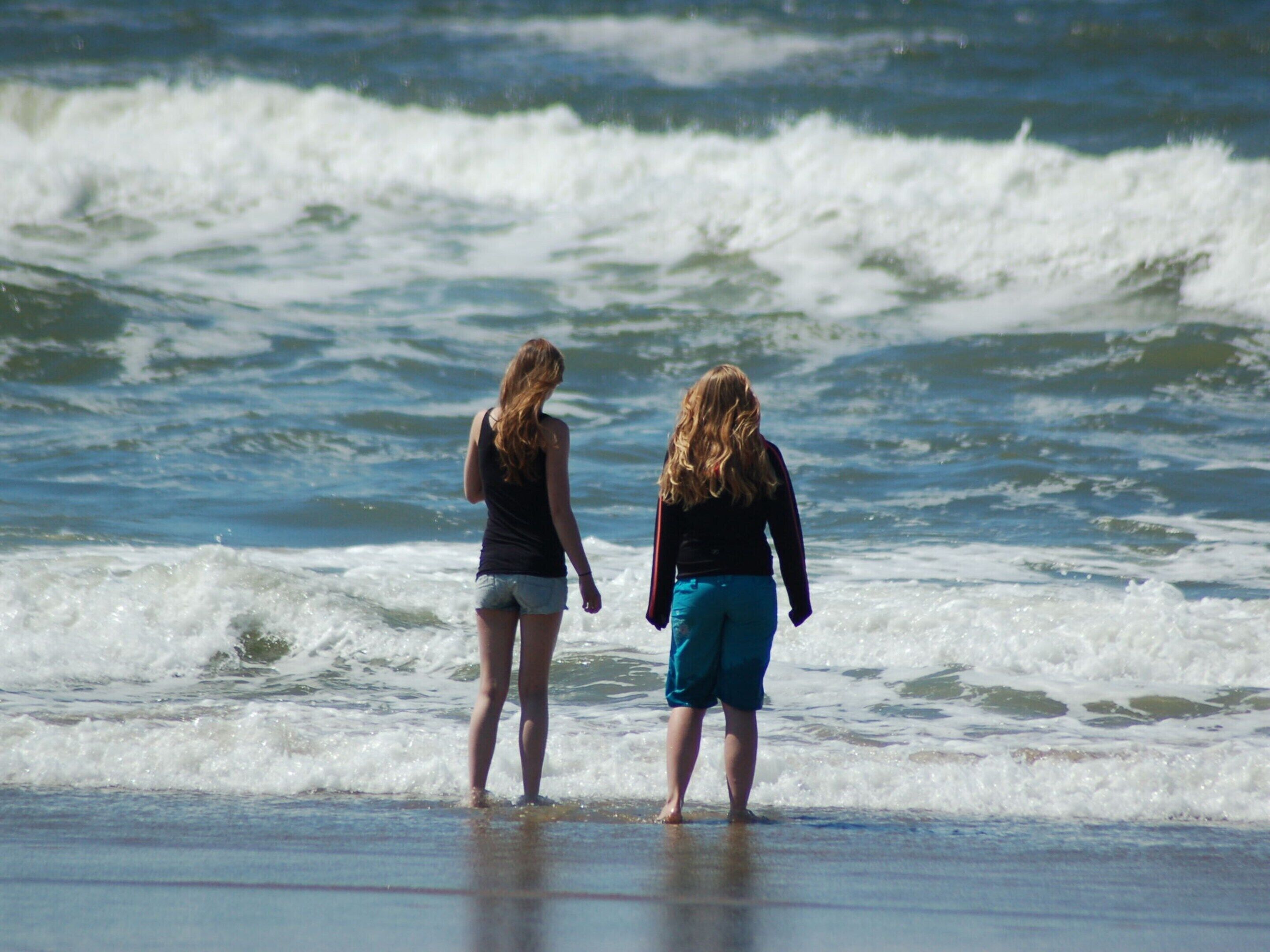 Two people standing at the beach with waves in the background.