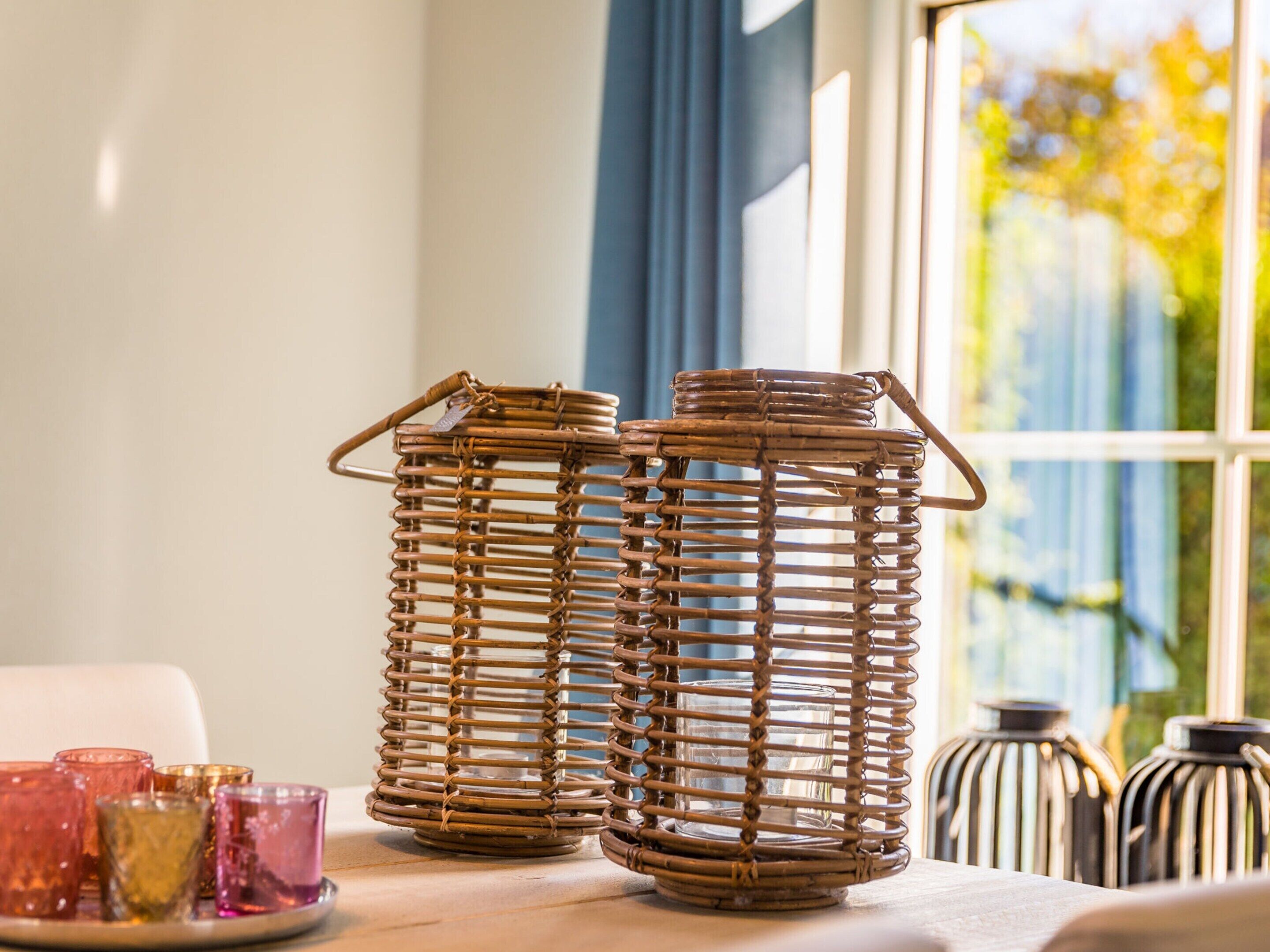Deux lanternes en osier sont posées sur une table, accompagnées de verres aux couleurs vives.
