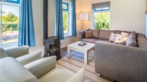A living room with a sofa, armchairs, a coffee table, a fireplace, and large windows with curtains. - Traditional Villa With two Bathrooms on Texel Near the Sea (De Koog)