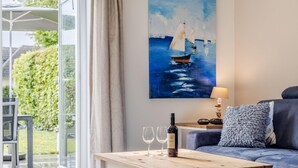 Ein modernes Wohnzimmer mit einem blauen Sofa, einem Holztisch mit einer Weinflasche und Gläsern sowie einem Bild von Segelbooten an der Wand.