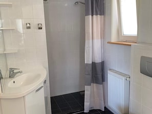 Een badkamer met een wit wastafelmeubel, een douche met een gestreept gordijn en een raam met een houten plankje.