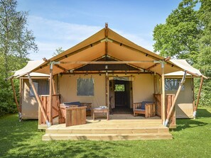 Eine Holzterrasse mit überdachter Sitzgruppe und einem zentralen Tisch, umgeben von einer Zelthallenkonstruktion.
