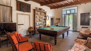 Een kamer met een pooltafel, oranje stoelen, een boekenkast en een houten plafond.