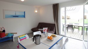 Moderni hotellihuone, jossa on ruokailutila, sohva, pöytä, jossa on vedenkeitin ja hedelmiä, sekä suuri ikkuna, josta on näkymä ulos.