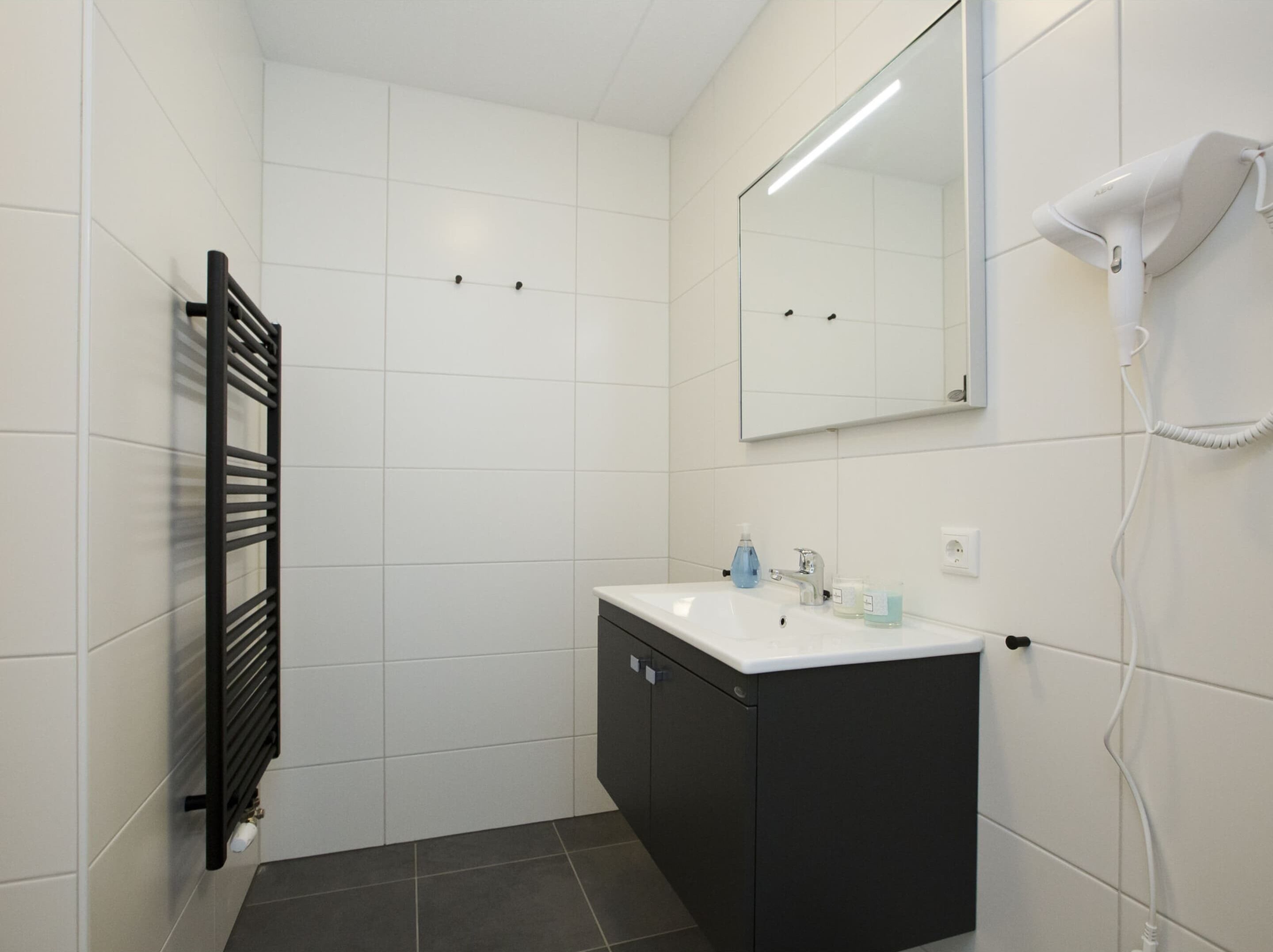 A bathroom with a black towel rack, a white sink with a mirror above it, and a hairdryer plugged in.