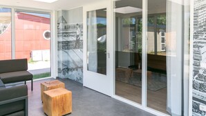 A modern interior with a grey floor, a wooden bench, and a glass door leading to an outdoor area. - Bungalow in Netherlands With Accessible Design ('s-Gravenzande)