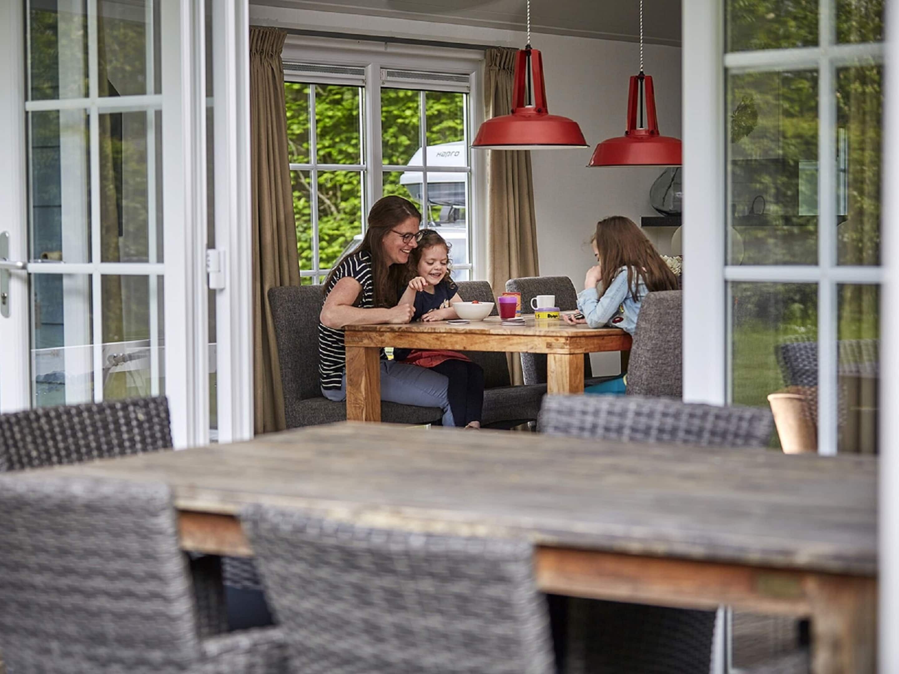 A dining area with a wooden table and chairs, large windows with curtains, and red pendant lights.