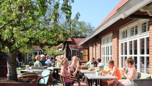 An outdoor seating area with tables and chairs, surrounded by brick buildings and trees. - Cozy Lodge in the Achterhoek (Winterswijk - Brinkheurne)