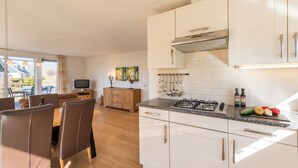 Une cuisine moderne avec des meubles blancs, une cuisinière à gaz et un coin repas comprenant une table et des chaises en bois.