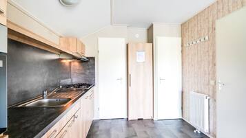 A modern kitchen with a stainless steel sink, wooden cabinets, and a black countertop. There are two white doors and a white radiator on the wall.