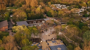 An aerial view of a residential area with a large building, a basketball court, and surrounding trees. - Villa in Kijkduin Near North Sea Beach (The Hague)