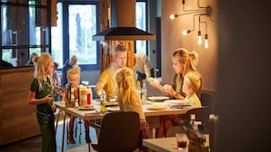 Een restaurant met een modern interieur, met een centrale eettafel omringd door stoelen, een bar en een groot raam dat natuurlijk licht binnenlaat.