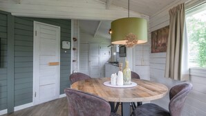 A dining area with a round wooden table, four chairs, a green pendant light, and a painting on the wall. - Apartment in Netherlands Near Nature Trails (Arcen)