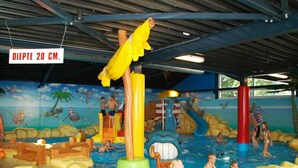 Een overdekt waterpark met glijbanen, opblaasbare attracties en een muurschildering van een tropisch landschap.