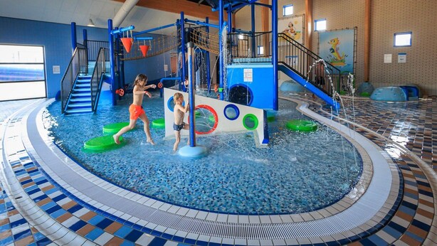 Un espace de jeux aquatiques intérieur comprenant des toboggans, des structures d’escalade et une piscine.