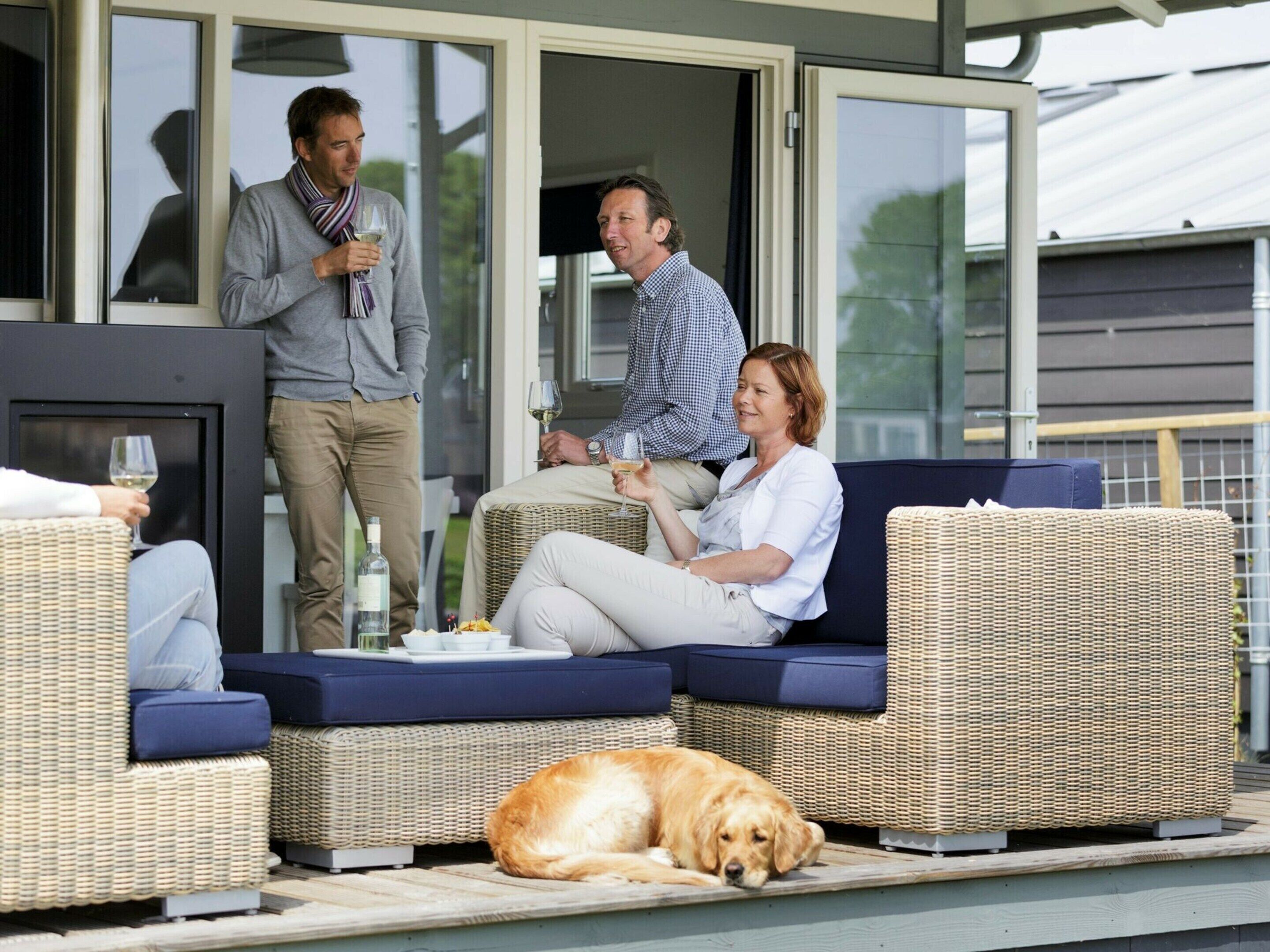 An outdoor seating area with wicker furniture, a glass table, and a dog lying on the floor.