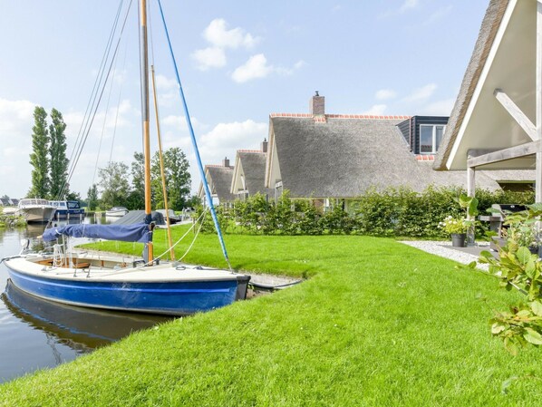 A canal-side property with a boat docked, a grassy lawn, and traditional houses with sloped roofs. - Modern Chalet Near Lake Sneek (Terkaple)