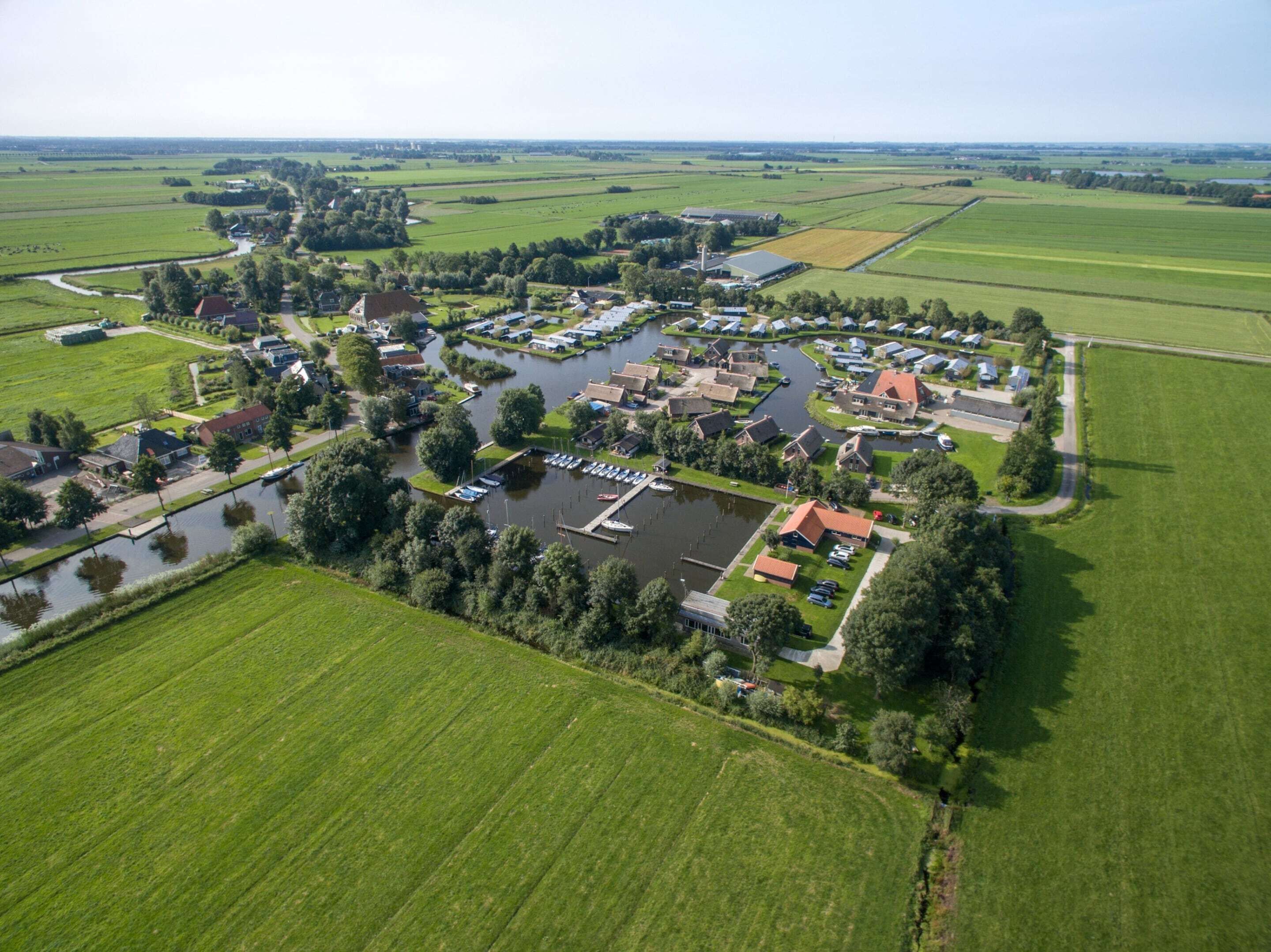 An aerial view of a rural village with houses, a canal, and boats docked at a marina.