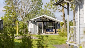 A modern house with a large glass door, a porch with seating, and a well-maintained lawn. - Modern Chalet Near Lake Sneek (Terkaple)