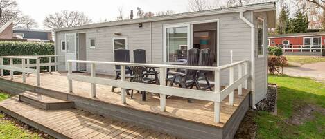 A small, single-story house with a deck, outdoor seating, and a covered patio area.