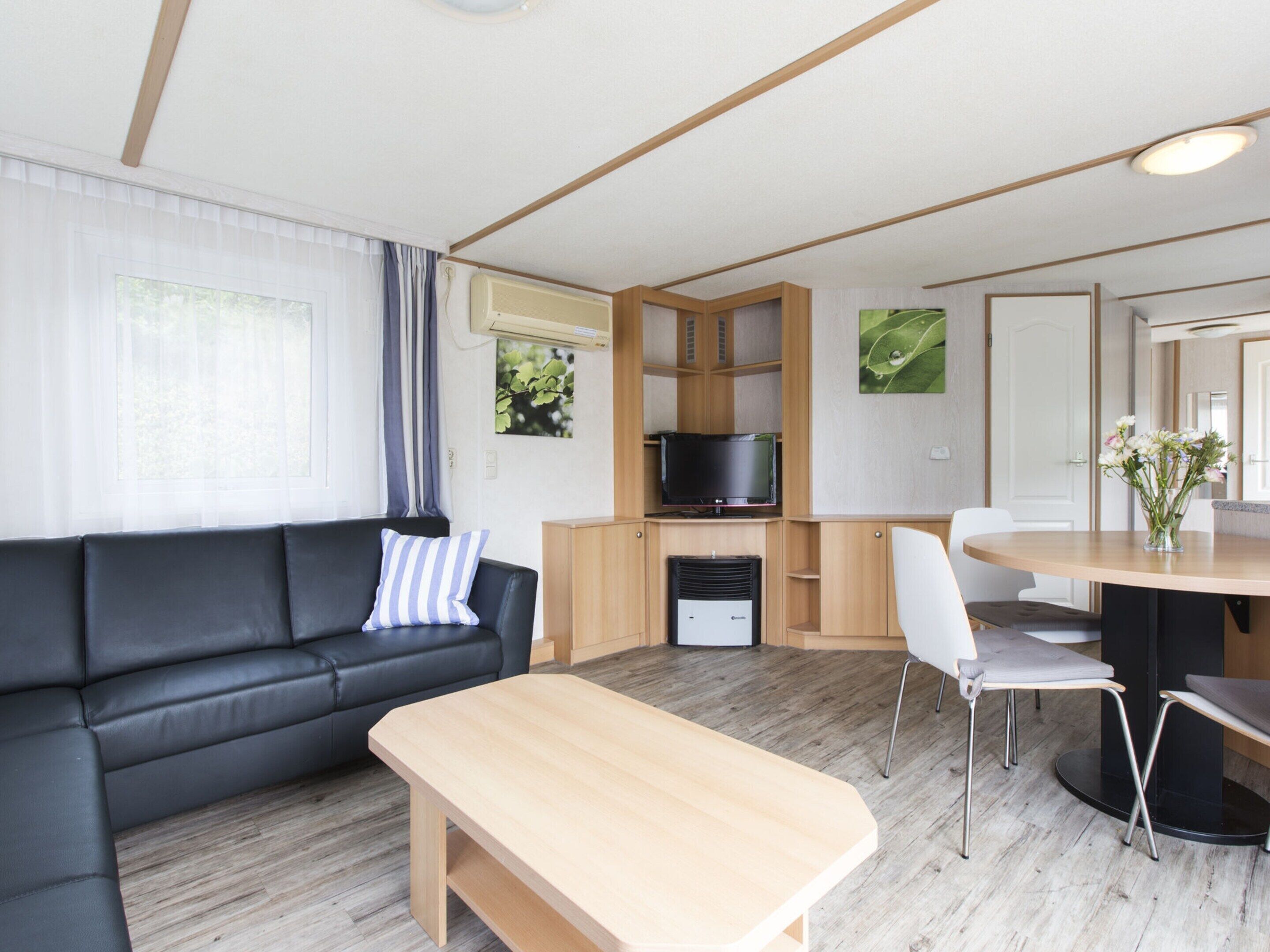 Een moderne woonkamer met een zwarte bank, een houten salontafel, een televisie en een eethoek met stoelen en een tafel.