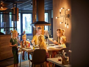 A restaurant with a modern interior, featuring a central dining table surrounded by chairs, a bar area, and a large window providing natural light. - Beautiful Villa in Limburg Near Lake (Roggel)