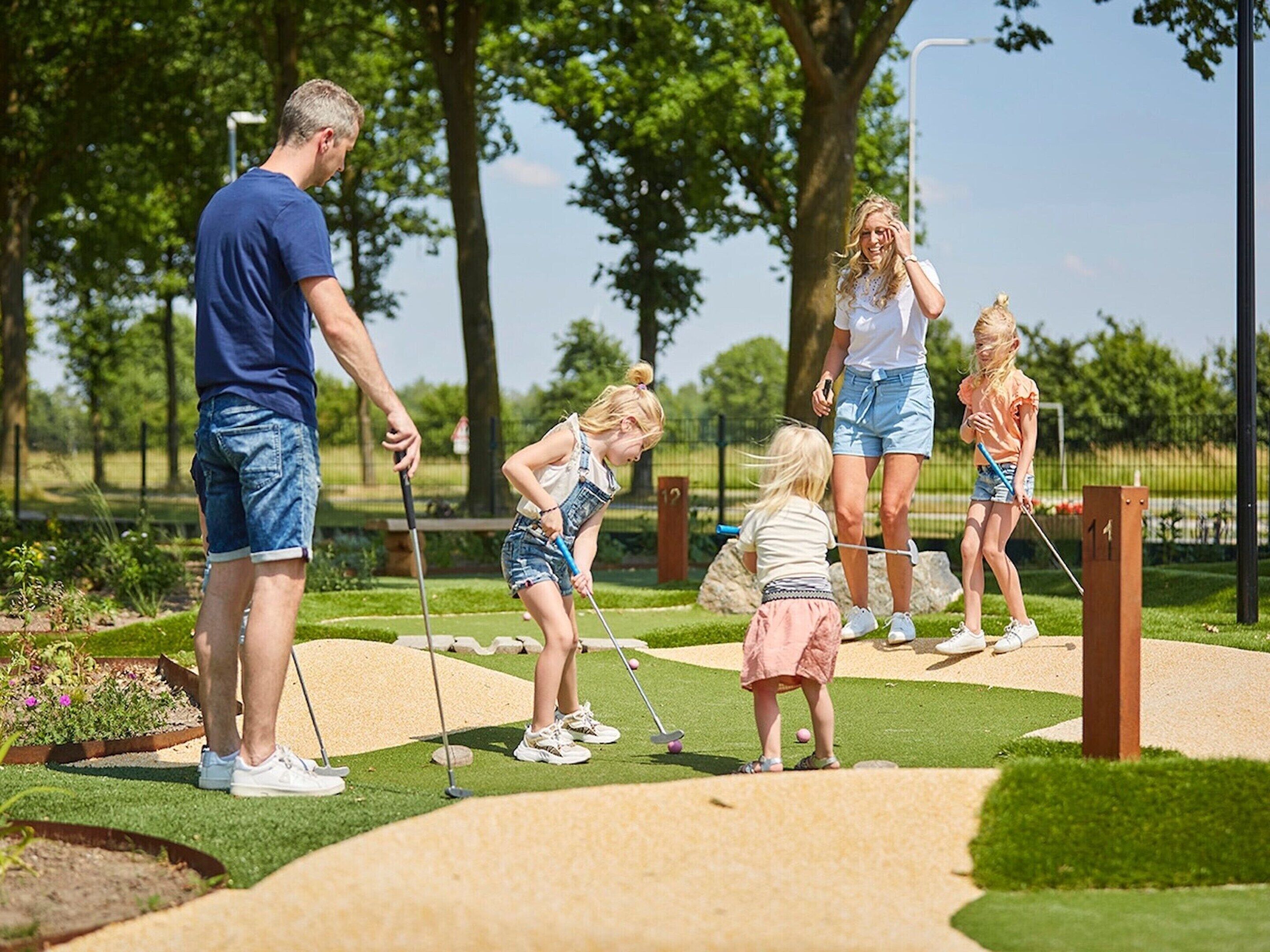 A family playing mini-golf on a well-maintained course with a clear sky and lush greenery in the background.