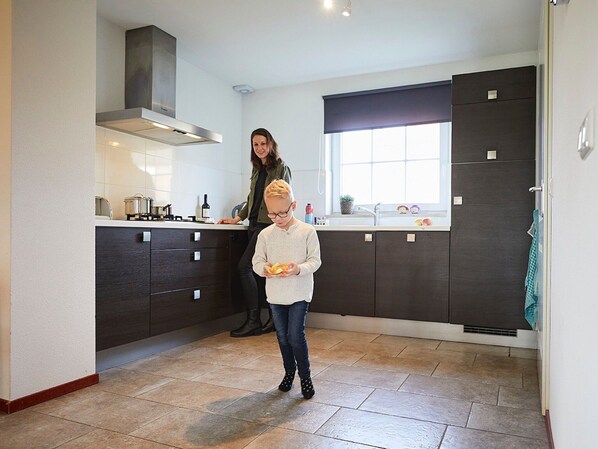Una cocina moderna con armarios oscuros, una campana extractora de acero inoxidable y un ventanal que proporciona luz natural.