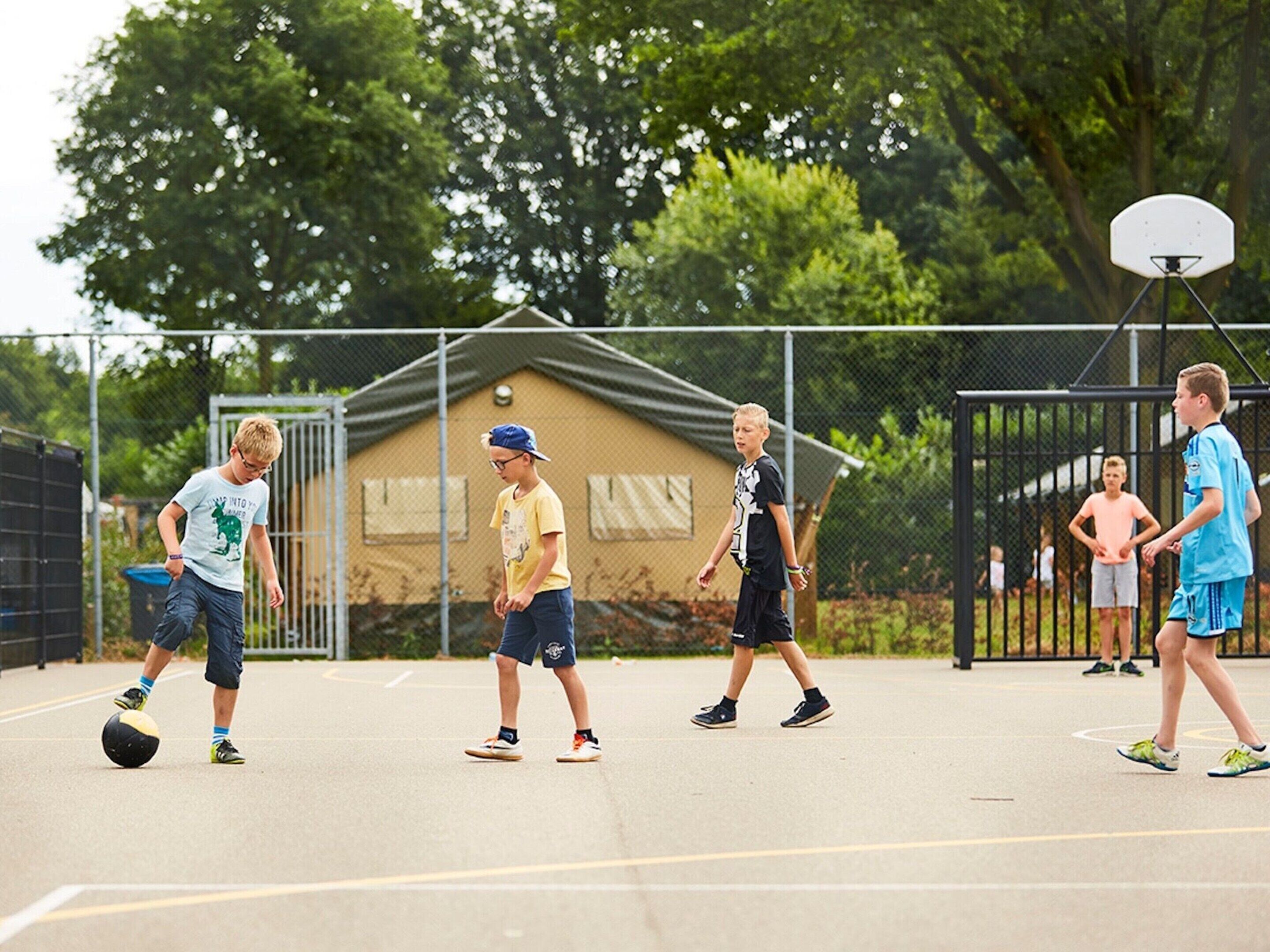A basketball court with a fence, trees, and a building in the background.