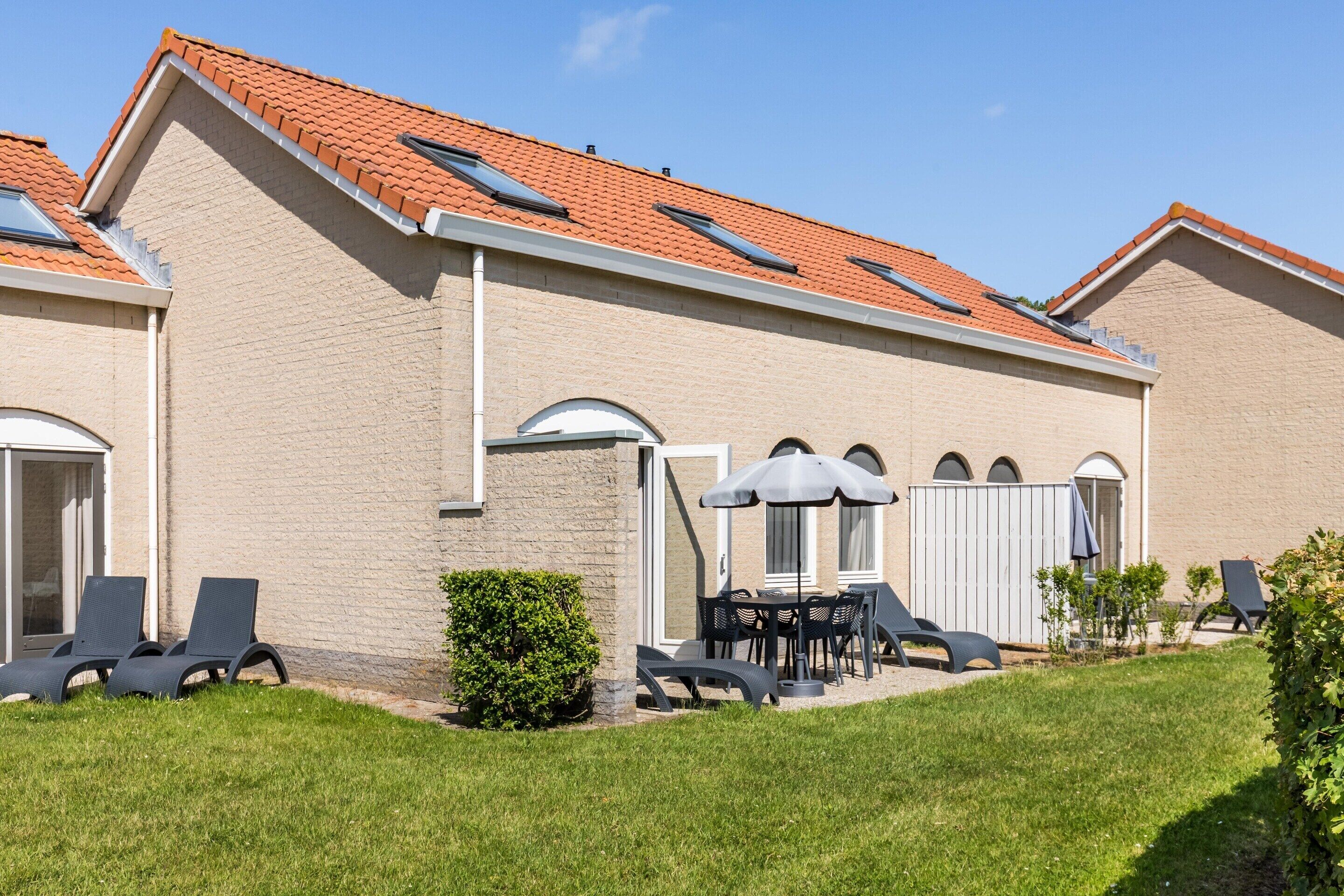A house with a tiled roof, a patio with a table and chairs, and a small garden.