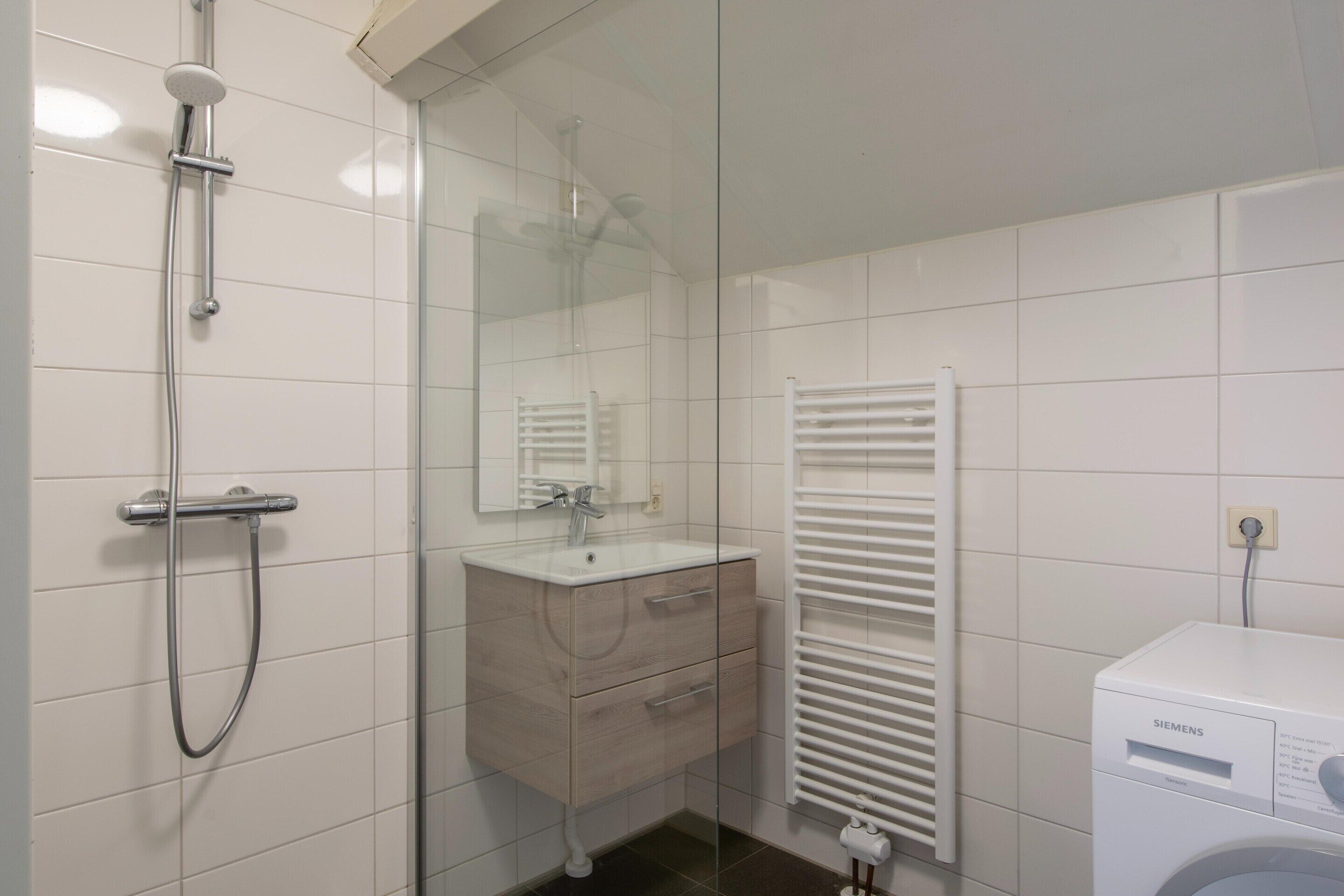 Et moderne badeværelse med en glasbrusekabine, et trækommode, en hvid radiator og en Siemens vaskemaskine.