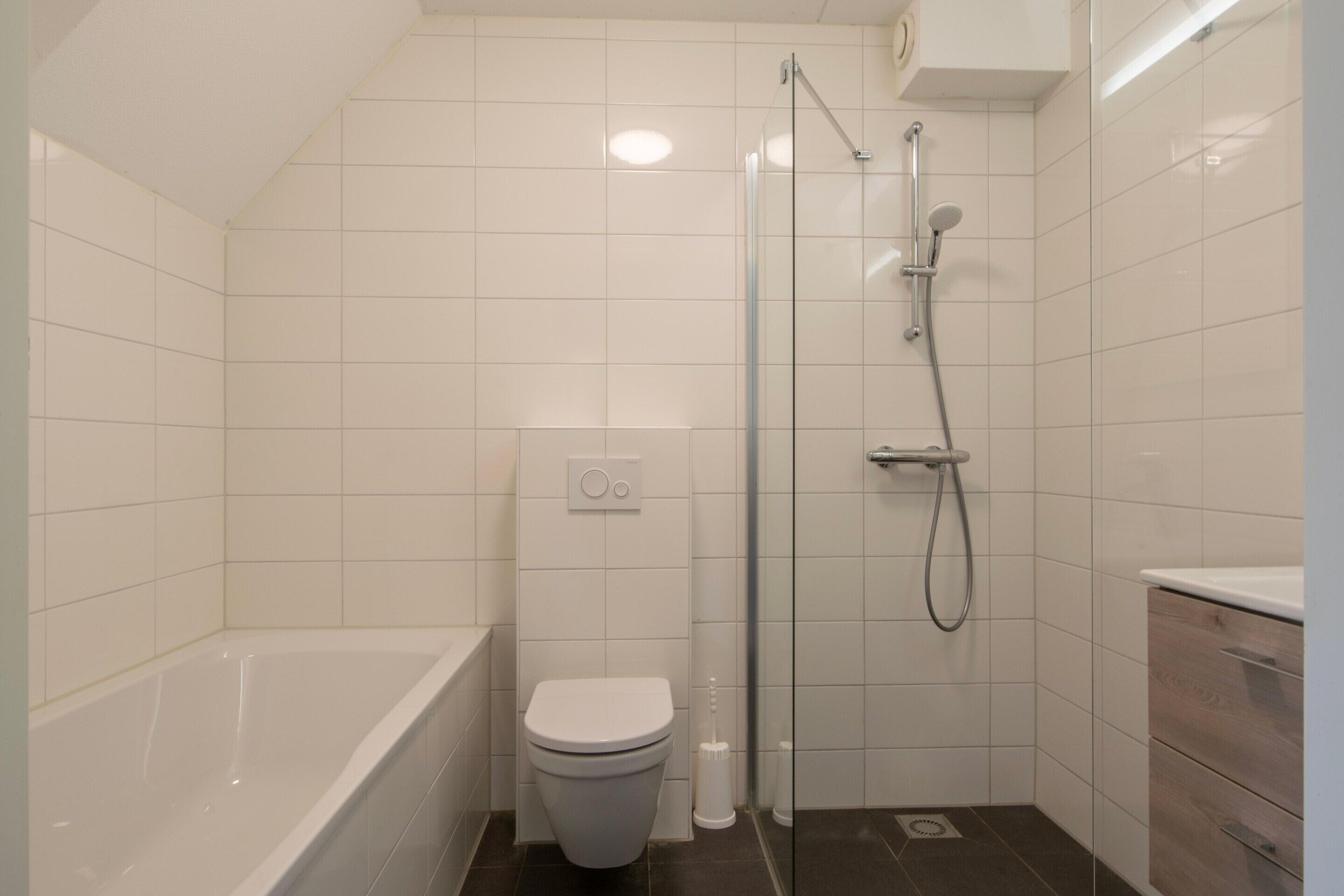 A modern bathroom with a bathtub, toilet, and glass-enclosed shower area.