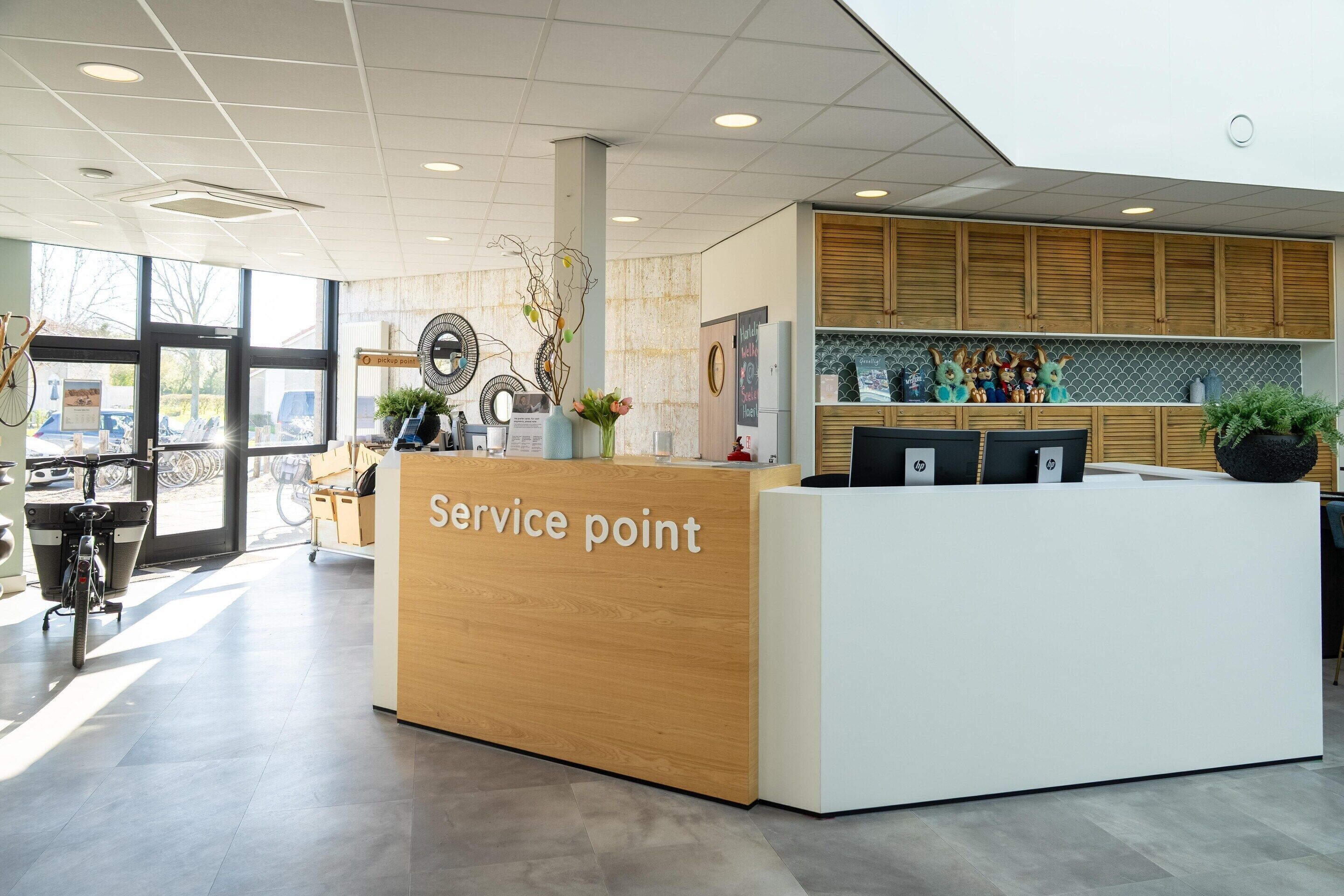 Un comptoir d’accueil avec un plan de travail en bois, un espace de réception blanc et un coin cuisine doté de meubles en bois et d’un pare-feu en carrelage.