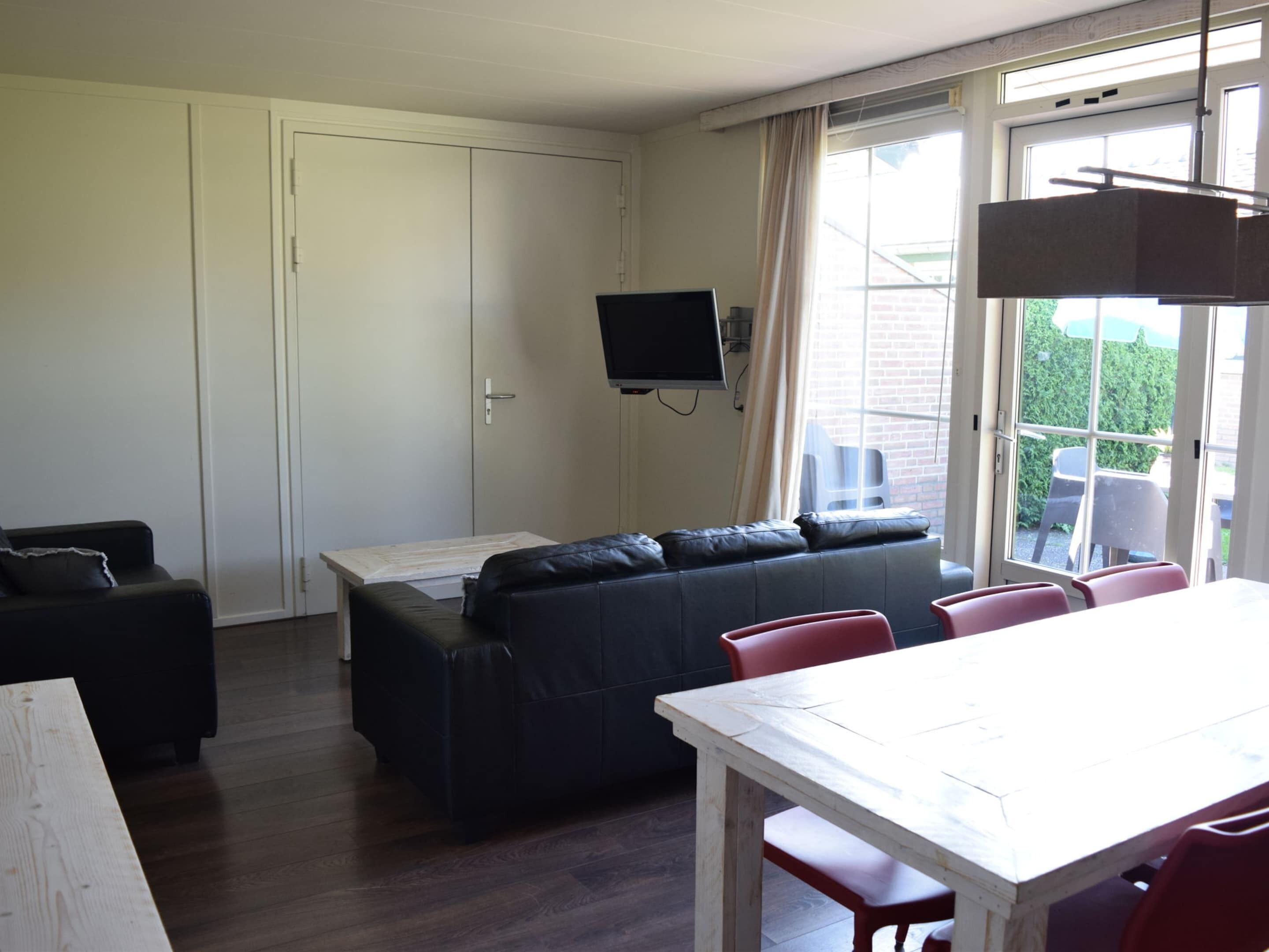 A living room with a sofa, a dining table, and a TV mounted on the wall.