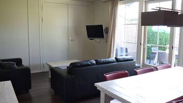 A living room with a sofa, a dining table, and a TV mounted on the wall.