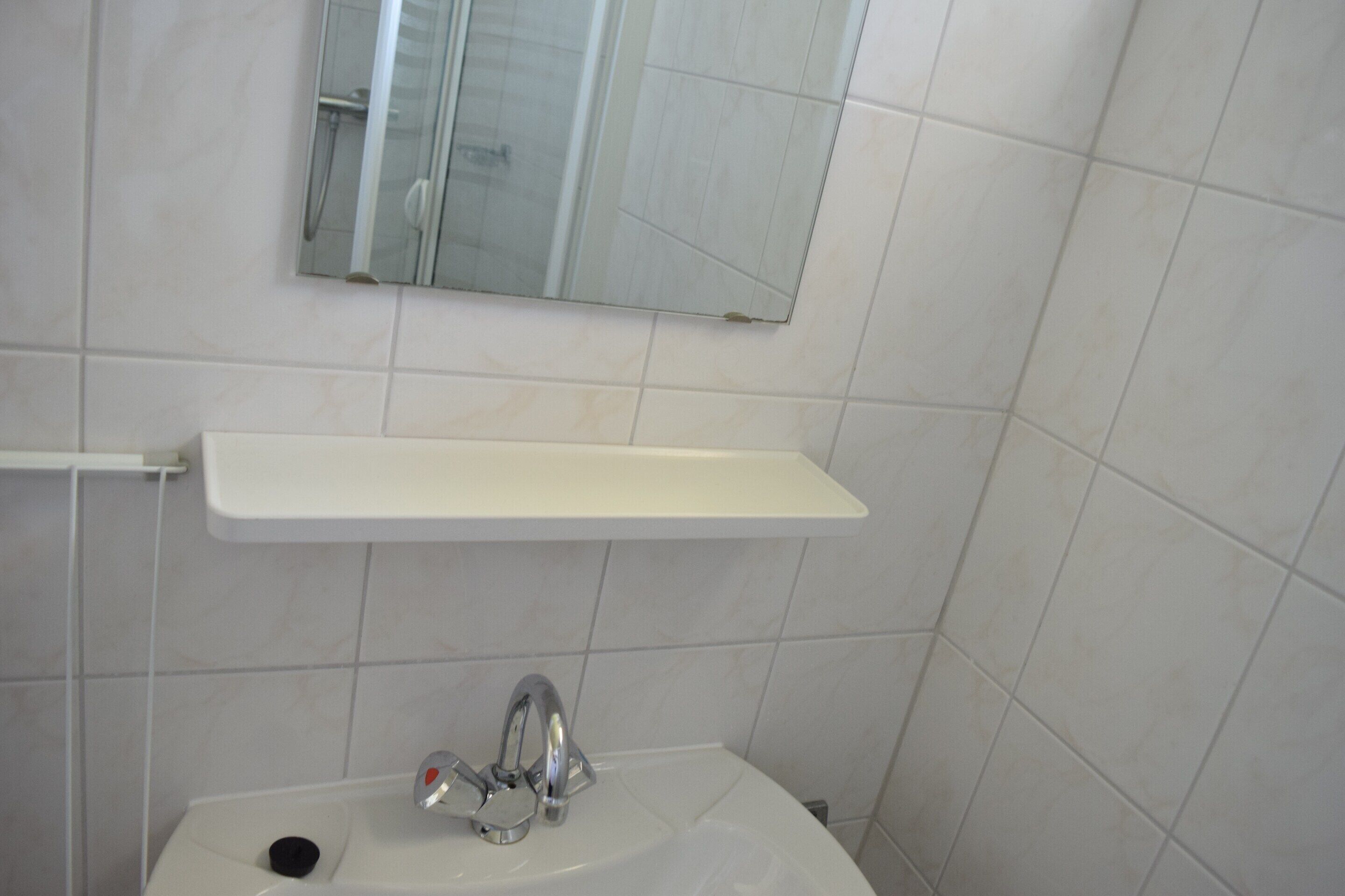 A bathroom with a white sink, a mirror, and a white shelf above it.