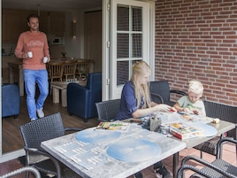 A dining area with a table set for two, a man walking in the background, and a brick wall.
