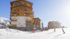 Een meerlaags houten gebouw met balkons, skipistes en een heldere lucht.