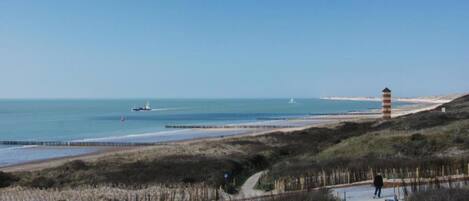 A coastal path with a lighthouse, beach, and a boat in the distance.