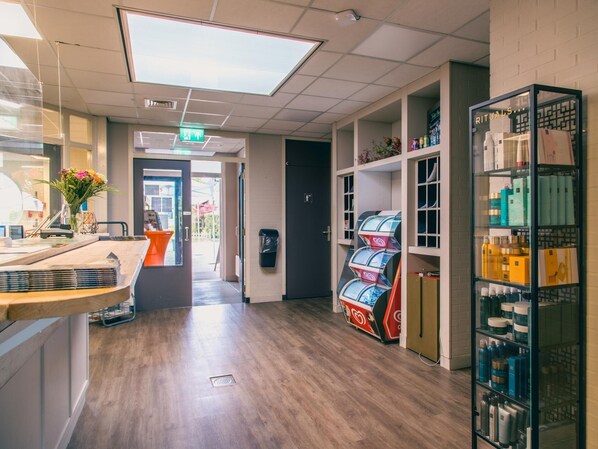 Un espace de vente moderne doté d’un plancher en bois, d’un espace d’accueil avec un comptoir et un vase de fleurs, ainsi que d’étagères remplies de divers produits.