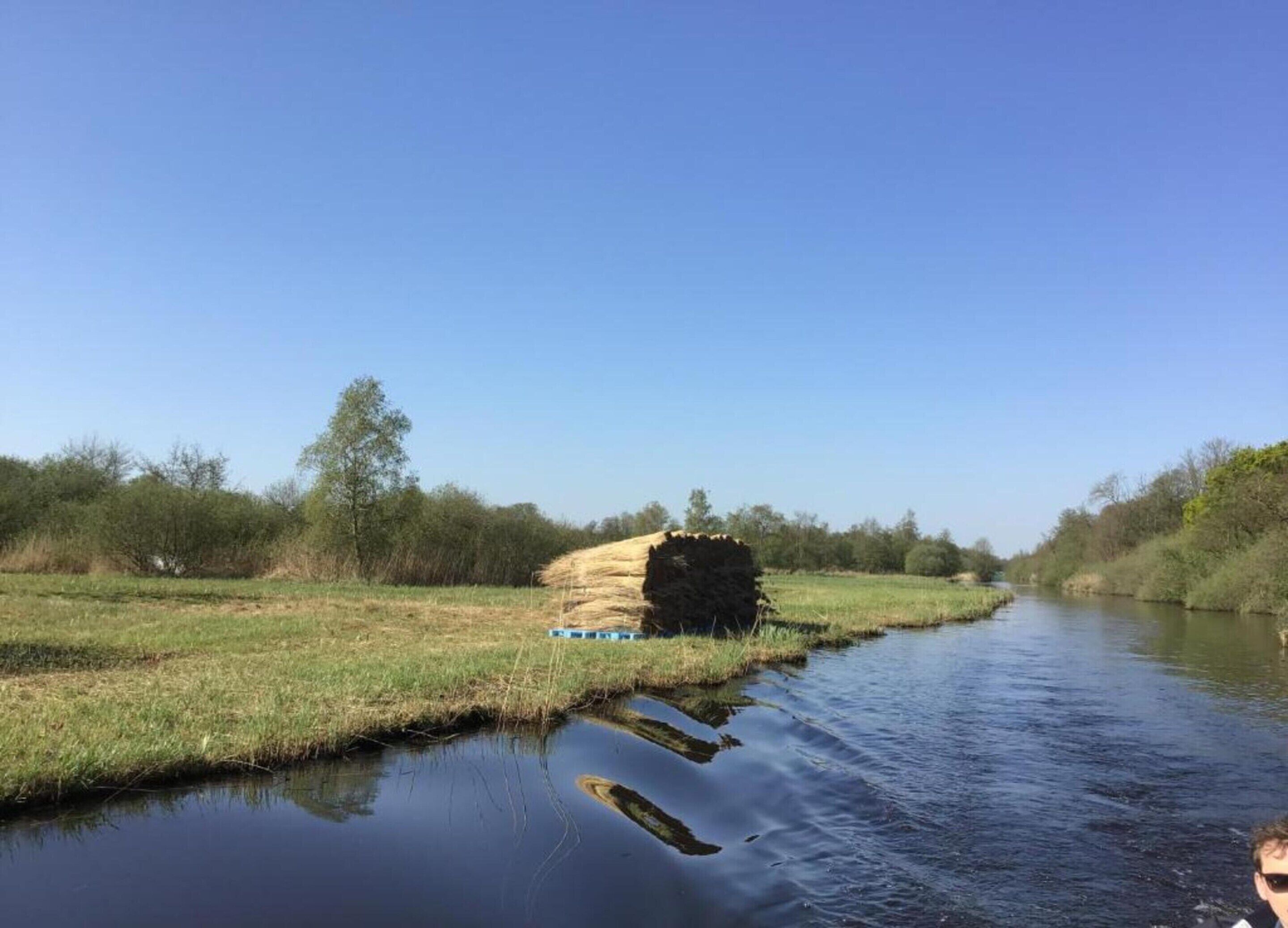 A river with a hay bale and a blue object on the bank.