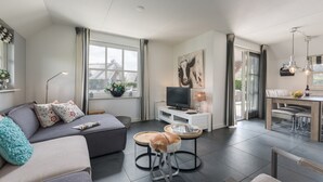 Ein modernes Wohnzimmer mit einer Couch, einem kleinen runden Tisch, einem Fernseher und einem Essbereich mit Tisch und Stühlen.