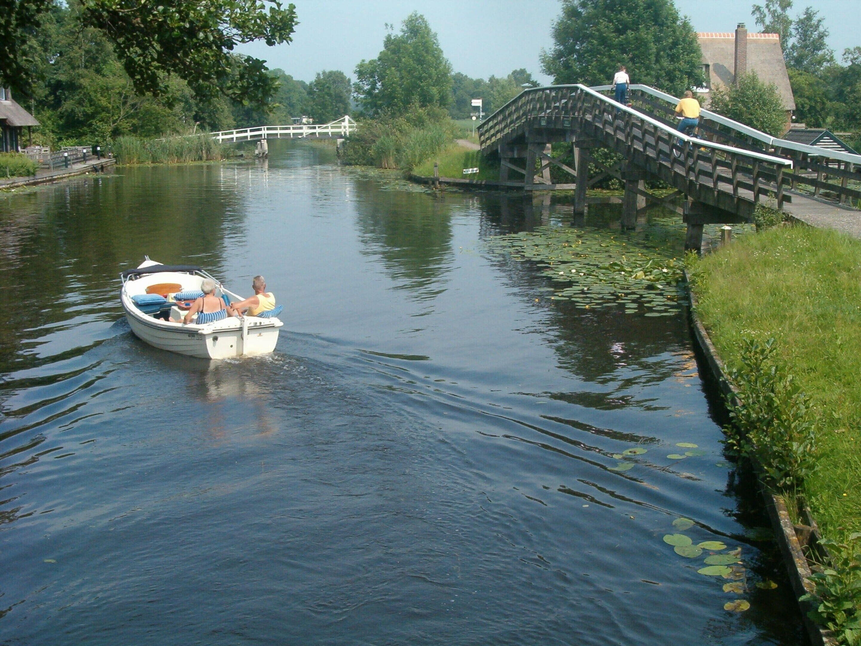 Un bateau sur une rivière paisible, avec un pont en bois en arrière-plan.