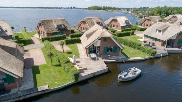 Ein Dorf am Seeufer mit reetgedeckten Häusern, einem Holzsteg und einem Boot.